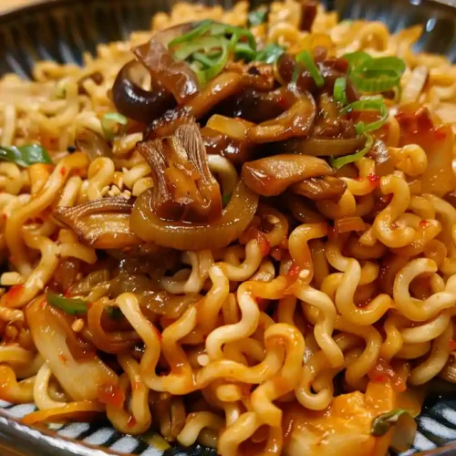 A bowl of saucy ramen noodles topped with mushrooms, chopped scallions, and vegetables.