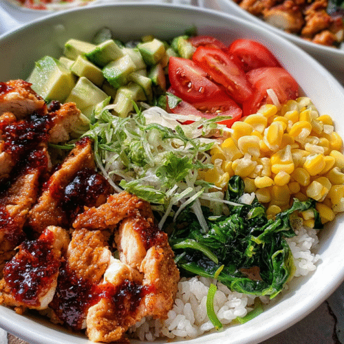 Colorful chicken bowl with grilled chicken, avocado, tomato, corn, greens, shredded lettuce, and rice, drizzled with chili sauce.