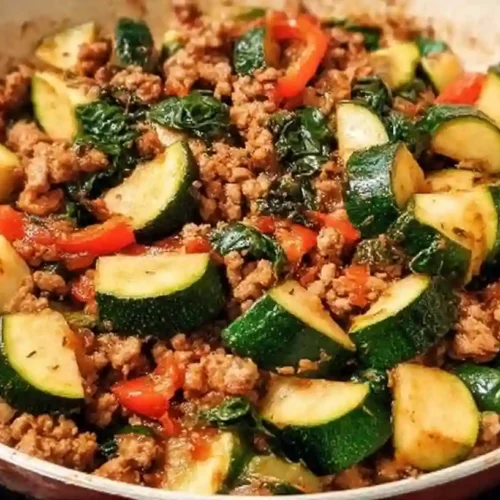 Ground turkey and zucchini skillet with red bell peppers, onions, and wilted spinach in a sauté pan.
