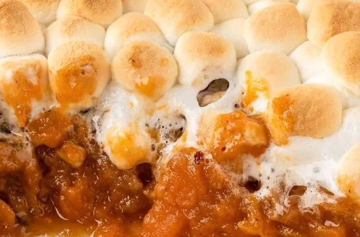 Sweet potato casserole topped with marshmallows and pecans, served in a dish.